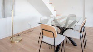 A modern dining area with a glass table, four chairs, a gold floor lamp, and a staircase with wooden steps. - Liiiving in Porto - City Design Apartment Q (Porto)
