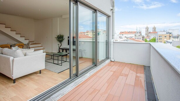 En moderne lejlighed med balkon, sofa, lille bord og trappe til en etage ovenpå.