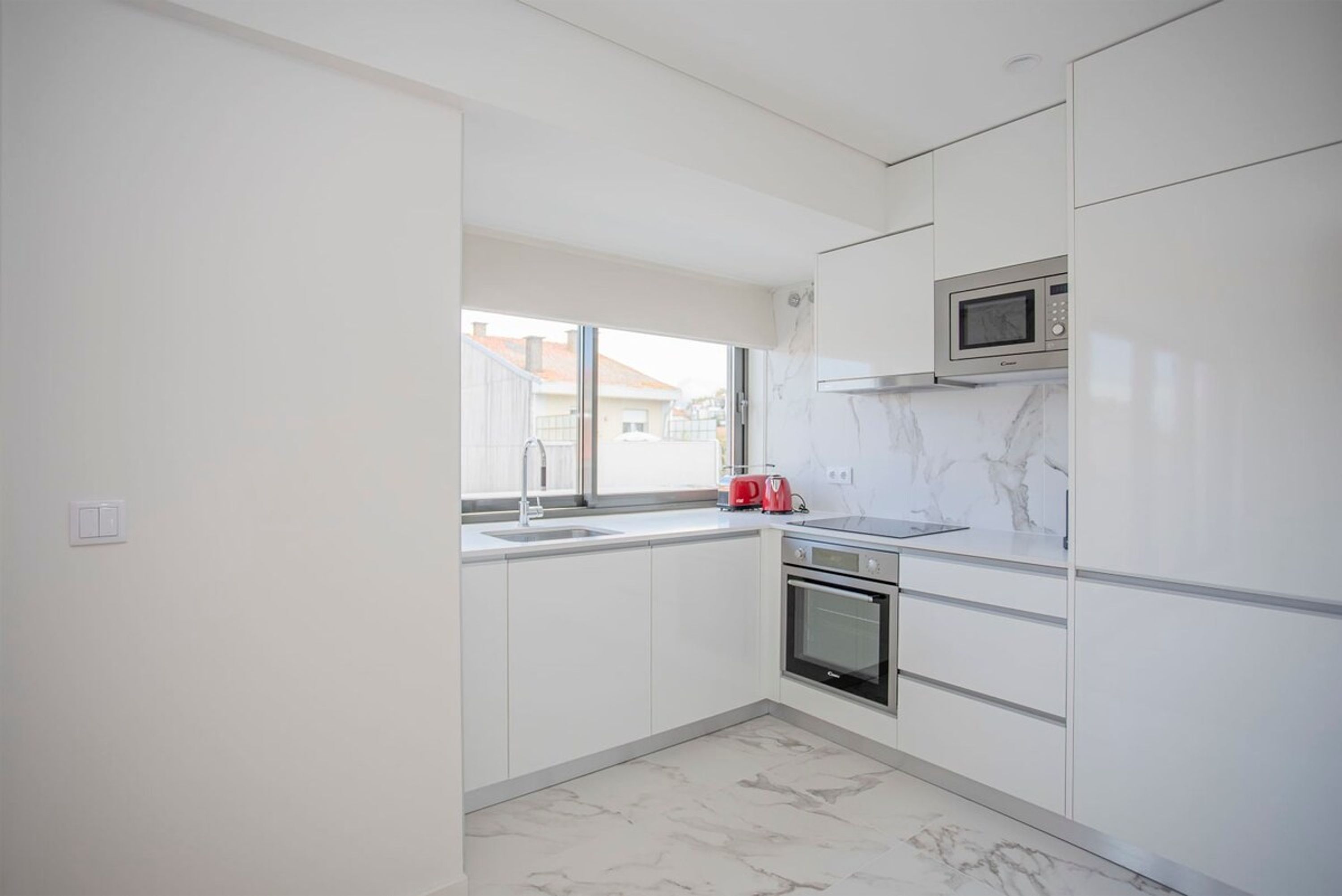 A modern kitchen with white cabinets, a microwave, an oven, and a red kettle.