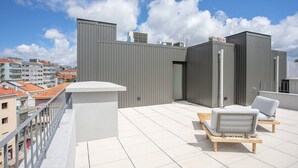 En tagterrasse med grå metalkonstruktioner, et hvidt gelænder og to liggestole.