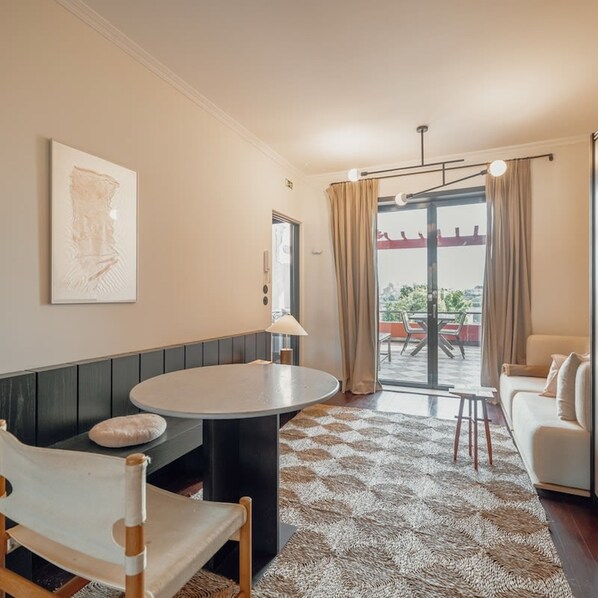 Una sala de estar moderna con una mesa redonda, un sofá, un sillón y un ventanal con cortinas.