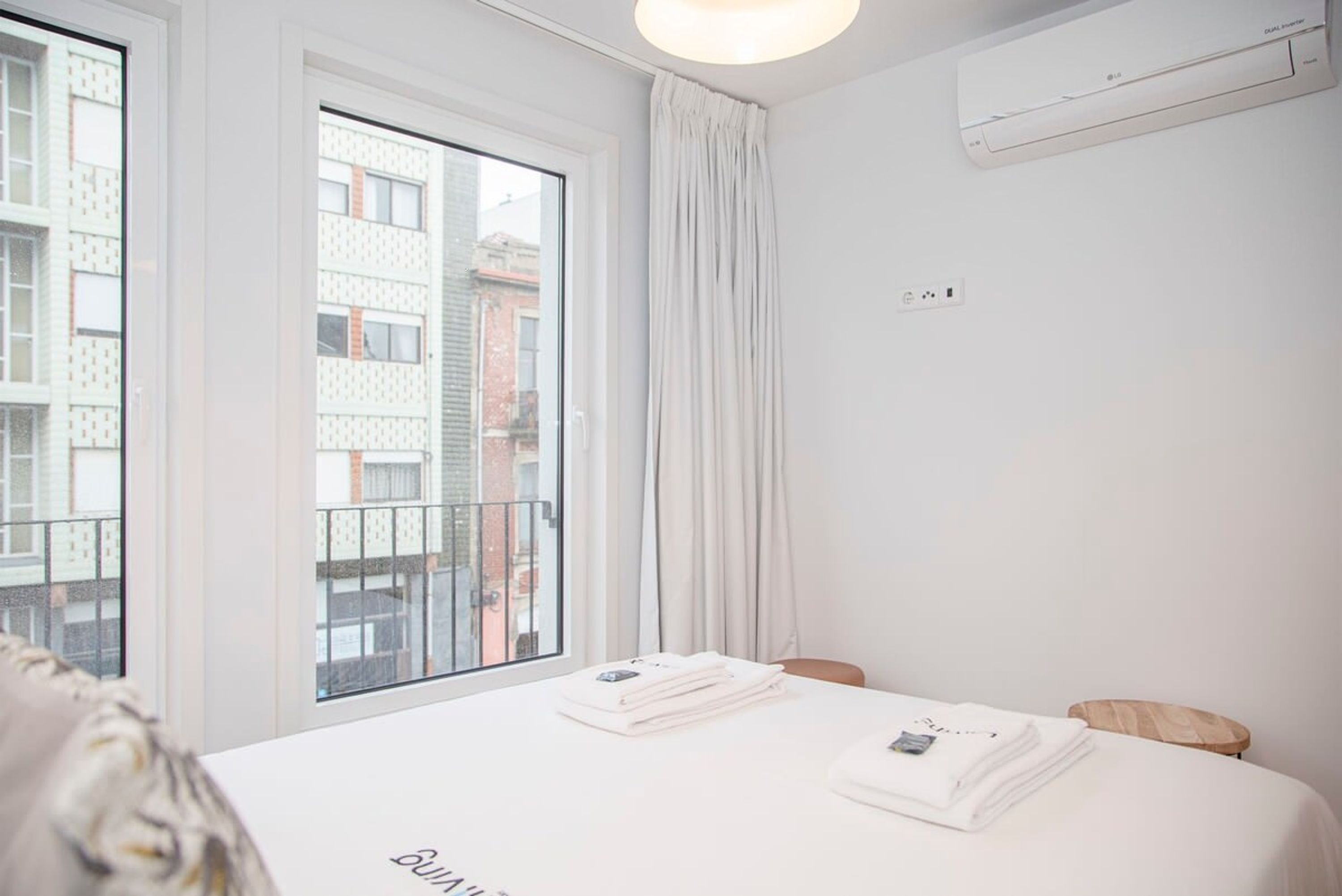 Habitación de hotel con un ventanal grande, cama con toallas ordenadas y aire acondicionado instalado en el techo.