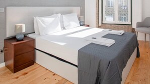 A modern bedroom with a large bed, a nightstand, a chair, and a window with a view of buildings. - Liiiving in Porto-mouzinho Residence Apartment 2F (Porto)