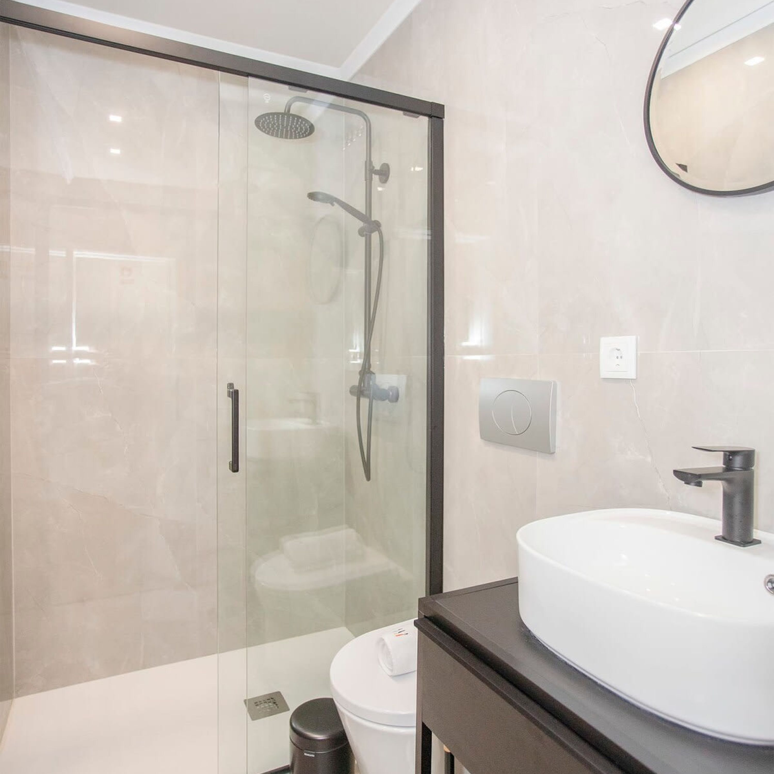 A modern bathroom with a glass-enclosed shower, a white sink, and a dark countertop.