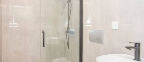 A modern bathroom with a glass-enclosed shower, a white sink, and a dark countertop.