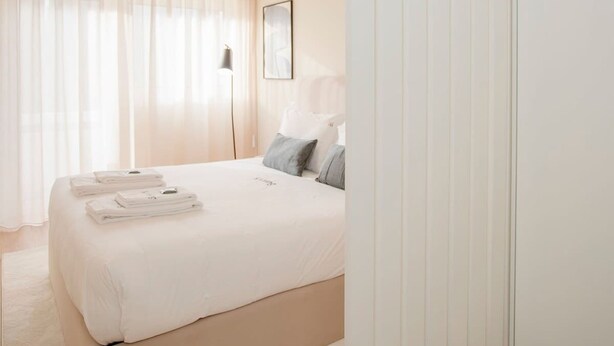 A modern bedroom with a large bed, a bedside table, a lamp, and a framed picture on the wall. - Liiiving in Porto - Uptown Pearl Apartment (Porto)