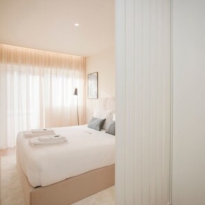 A modern bedroom with a large bed, a bedside table, a lamp, and a framed picture on the wall. - Liiiving in Porto - Uptown Pearl Apartment (Porto)