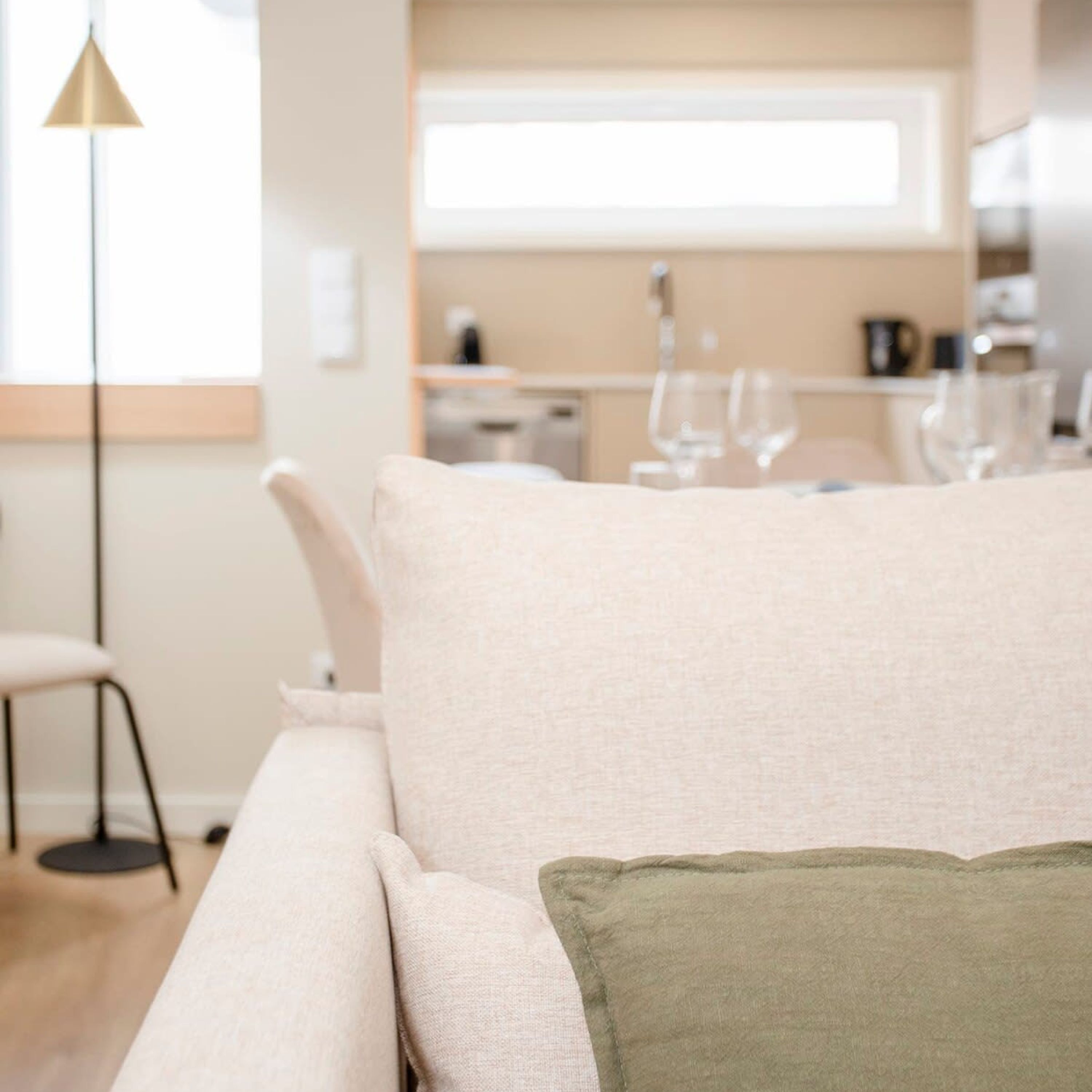 A modern living room with a sofa, a green accent pillow, a floor lamp, and a view of a kitchen and dining area.