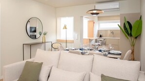 A modern living room with a sofa, dining table, and kitchen area in the background. - Liiiving in Porto - Uptown Pearl Apartment (Porto)
