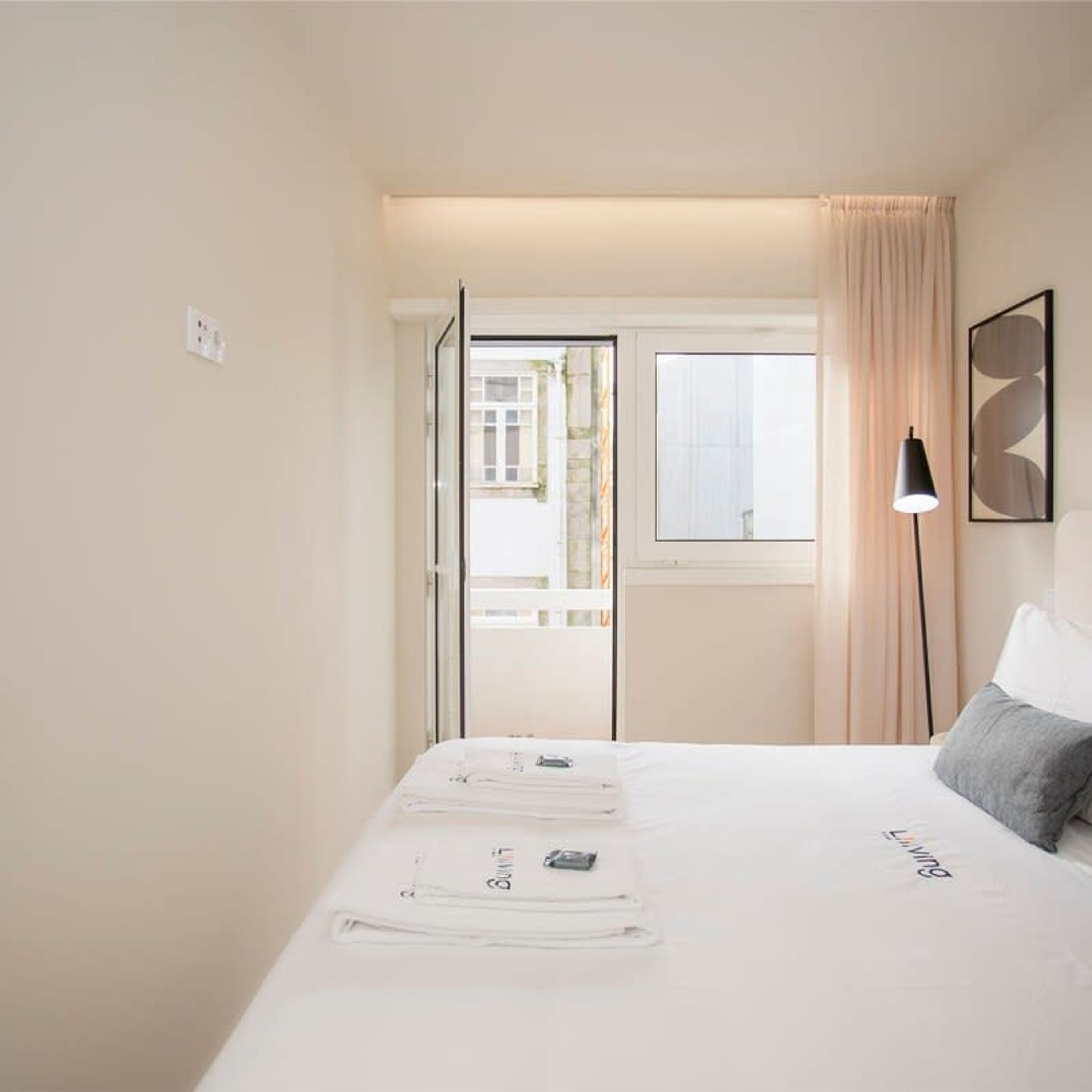 A hotel room with a bed, a window with curtains, a bedside lamp, and a framed abstract artwork on the wall.