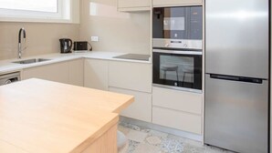 A modern kitchen with a built-in oven, a stainless steel refrigerator, and a window above the sink. - Liiiving in Porto - Uptown Pearl Apartment (Porto)