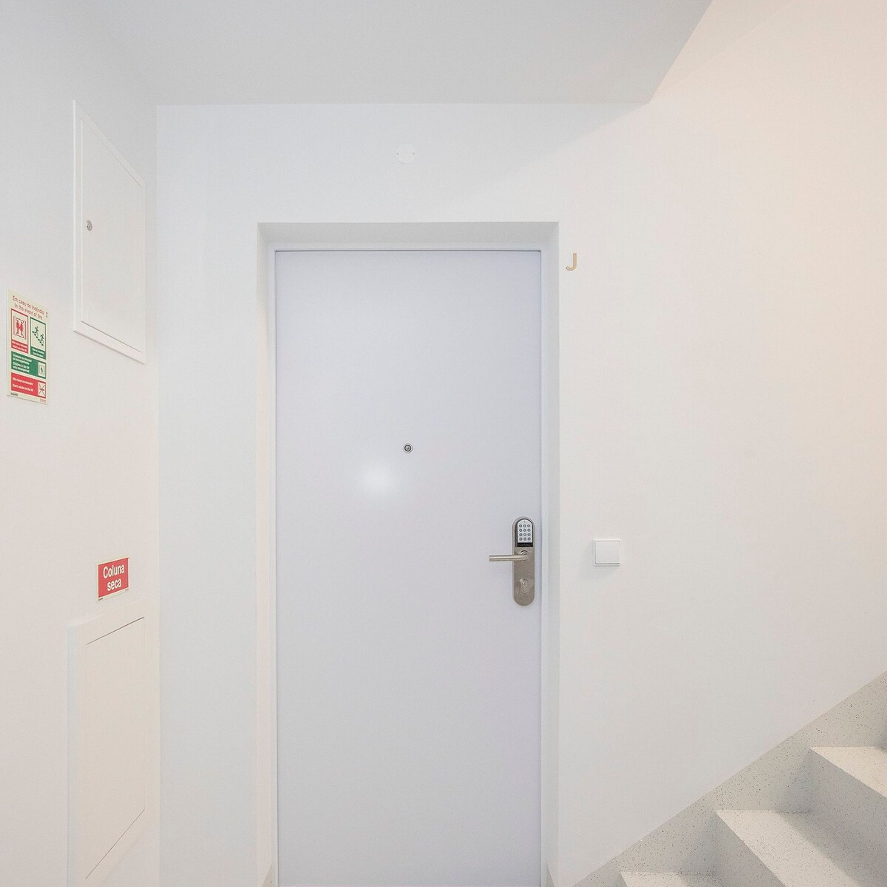 A white door with a keyhole and a handle, a small sign on the wall to the left, and a staircase to the right.