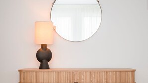 A wooden console table with a round mirror above it, a lamp on the table, and a wall-mounted light fixture. - Liiiving in Porto - Modern Glam Apartment J (Porto)