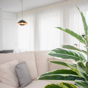 A modern living room with a beige sofa, a large green plant, and a pendant light. - Liiiving in Porto - Modern Glam Apartment J (Porto)