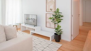 A modern living room with a sofa, a TV on a stand, a potted plant, and artwork on the wall. - Liiiving in Porto - Modern Glam Apartment J (Porto)