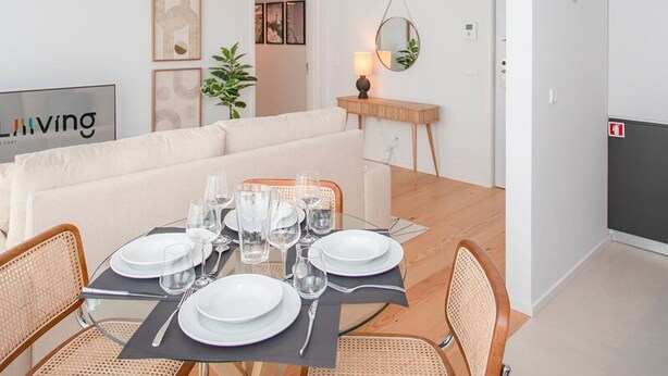 A dining area with a table set for four, a sofa, and a hanging light fixture. - Liiiving in Porto - Modern Glam Apartment J (Porto)
