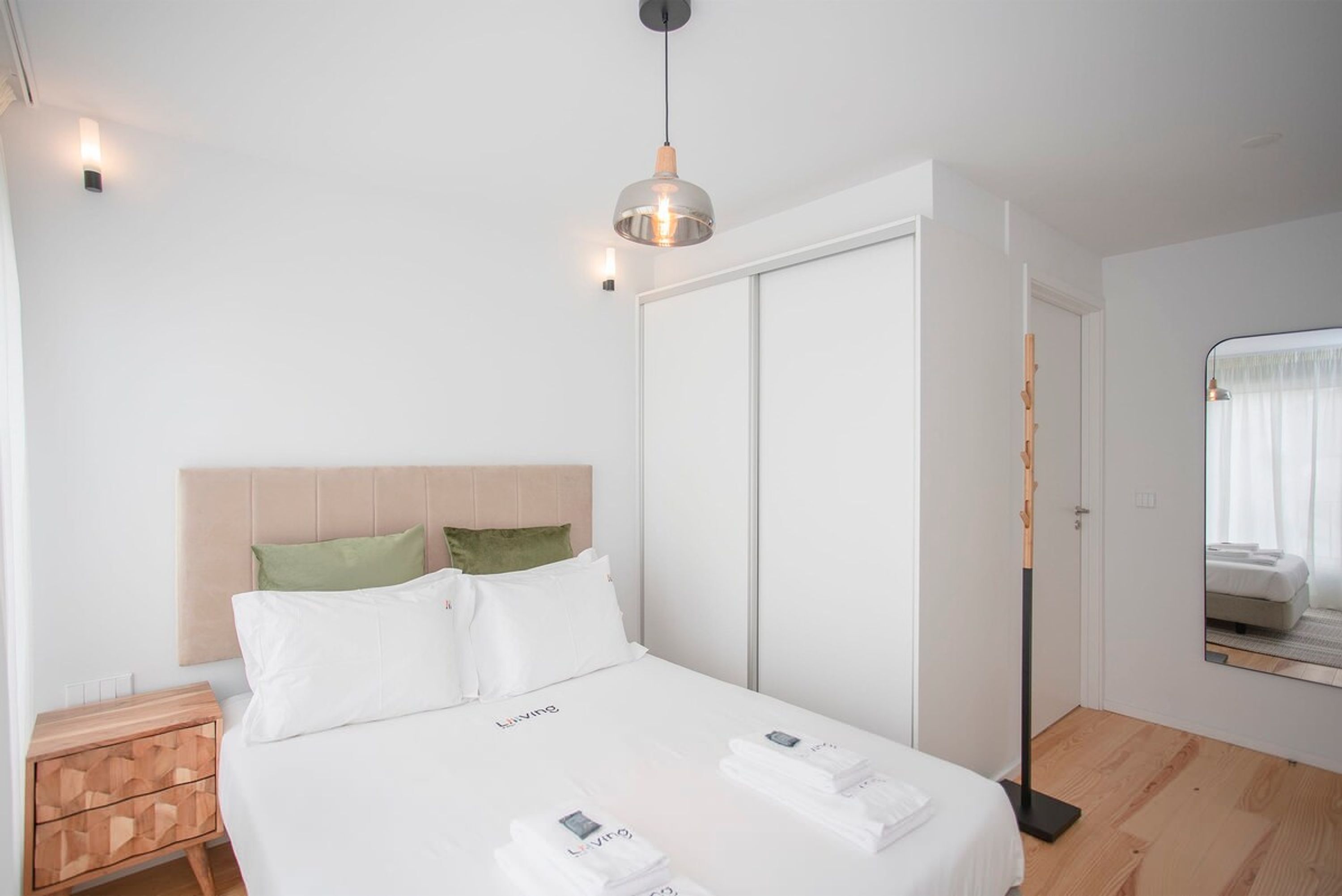 Una habitación de hotel con una cama, una mesita de noche, un espejo y un armario.