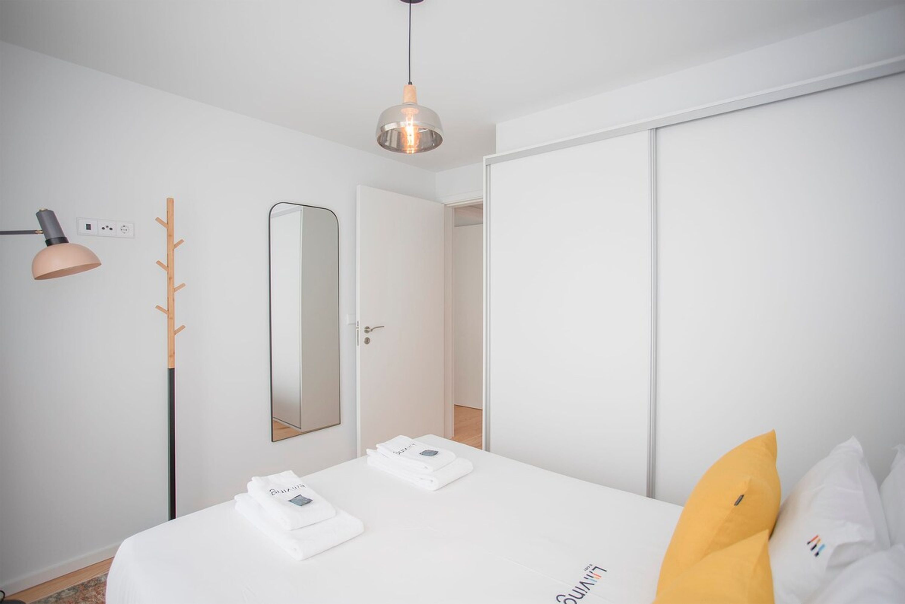 Ein Hotelzimmer mit Bett, Nachttischlampe, Kleiderständer, Spiegel und Kleiderschrank.