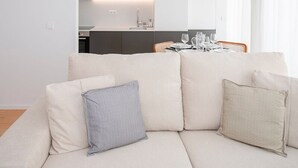 A modern living room with a sofa, a dining table set for four, and a kitchen in the background. - Liiiving in Porto - Modern Glam Apartment J (Porto)