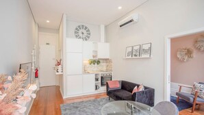 A modern living room with a sofa, a glass coffee table, and a kitchen area with cabinets and a clock. - Liiiving in Porto - Chic Sweet Home (Porto)