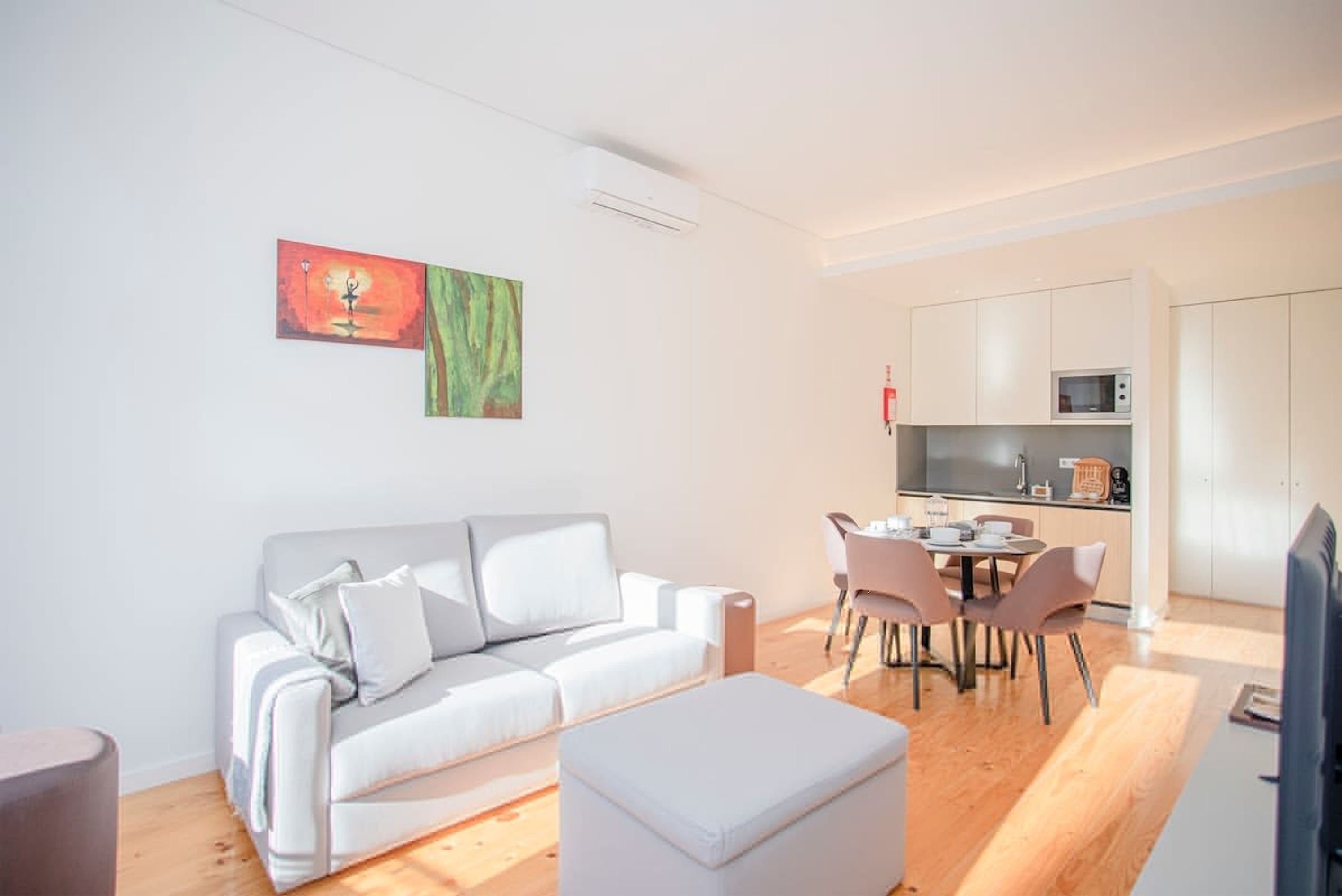 A modern living room with a white sofa, a dining table with chairs, and a kitchen area with cabinets and a microwave.