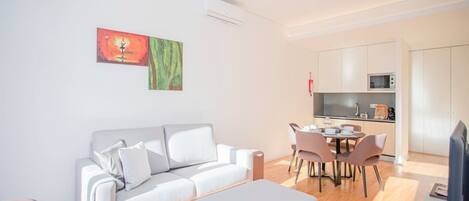 A modern living room with a white sofa, a dining table with chairs, and a kitchen area with cabinets and a microwave.