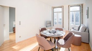 A modern living room with a dining area, large windows, and a view of buildings. - Liiiving in Porto-mouzinho Residence Apartment 3F (Porto)