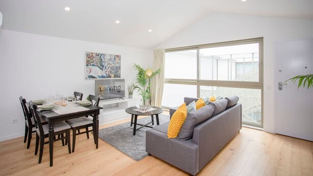 A modern living room with a dining area, a grey sofa, and a large window with a view. - NAX Apartment G by Liiiving (Porto)