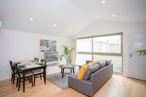En moderne stue med spiseplads, en grå sofa og et stort vindue med udsigt.