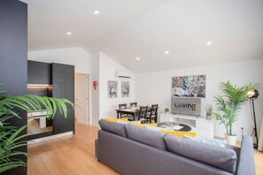 Un salon moderne avec un canapé gris, une table à manger et un téléviseur fixé au mur.