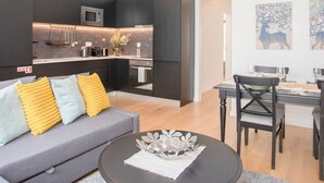 A modern living room with a grey sofa, a dining table with chairs, and a kitchen area with dark cabinets and a microwave. - NAX Apartment G by Liiiving (Porto)
