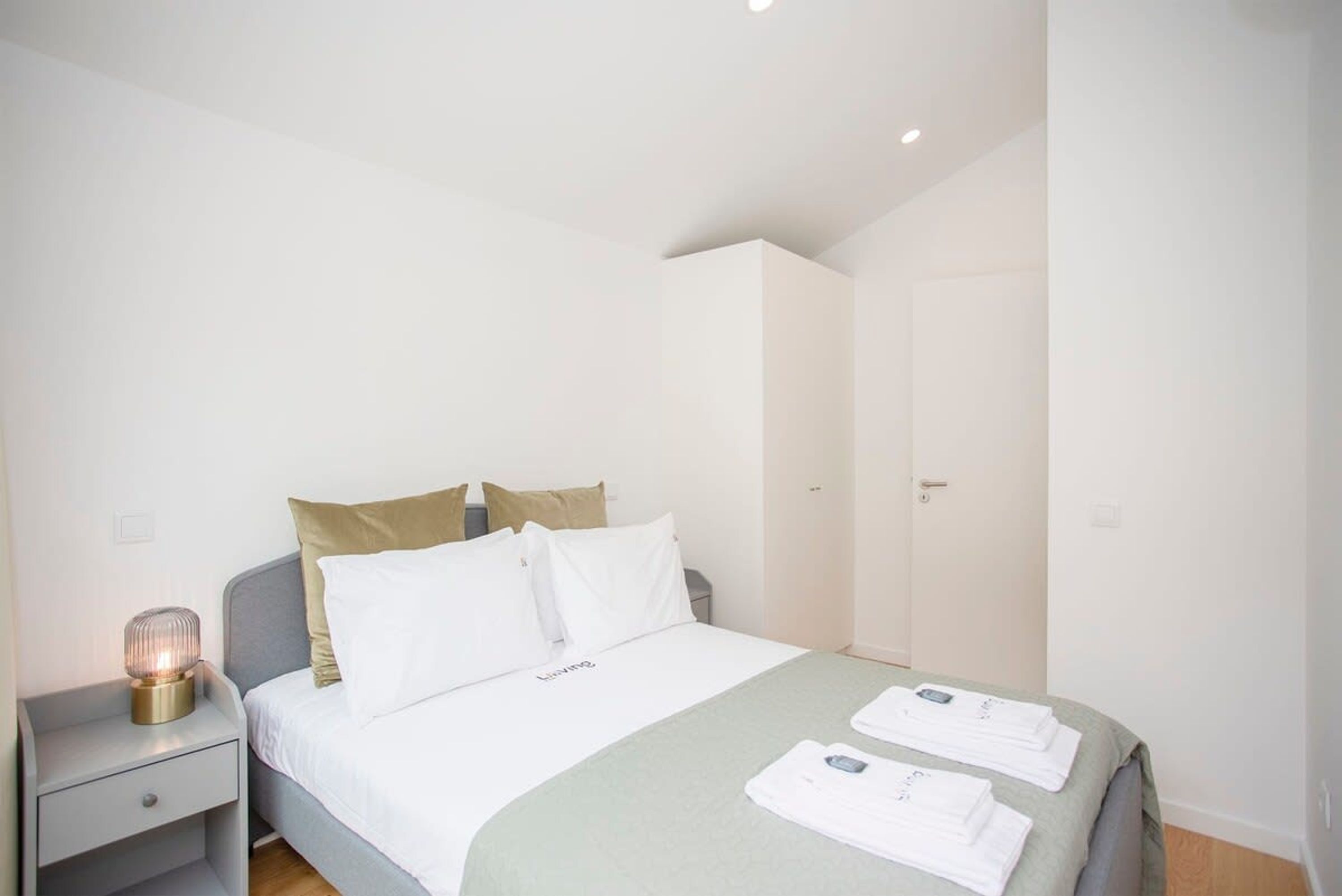 Een verzorgde hotelkamer met een bed, nachtkastje met een lamp en een kledingkast.