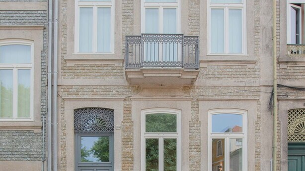 A multi-story building with a symmetrical facade, featuring a central balcony with ornate metal railings, a grey door with decorative glass panels, and multiple windows with white frames. - Liiiving in Porto - Haven Pool Apartment (Porto)