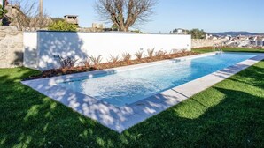 A swimming pool with a clear view of the surrounding landscape, a white wall, and a tree. - Liiiving in Porto - Haven Pool Apartment (Porto)