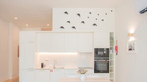 A modern kitchen with white cabinets, a dining area with a table and chairs, and a wall with bird decals. - Liiiving in Porto - Haven Pool Apartment (Porto)