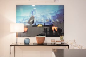 Une chambre moderne avec un grand tableau abstrait, un bureau avec une lampe, un vase bleu et un pot en terre cuite.