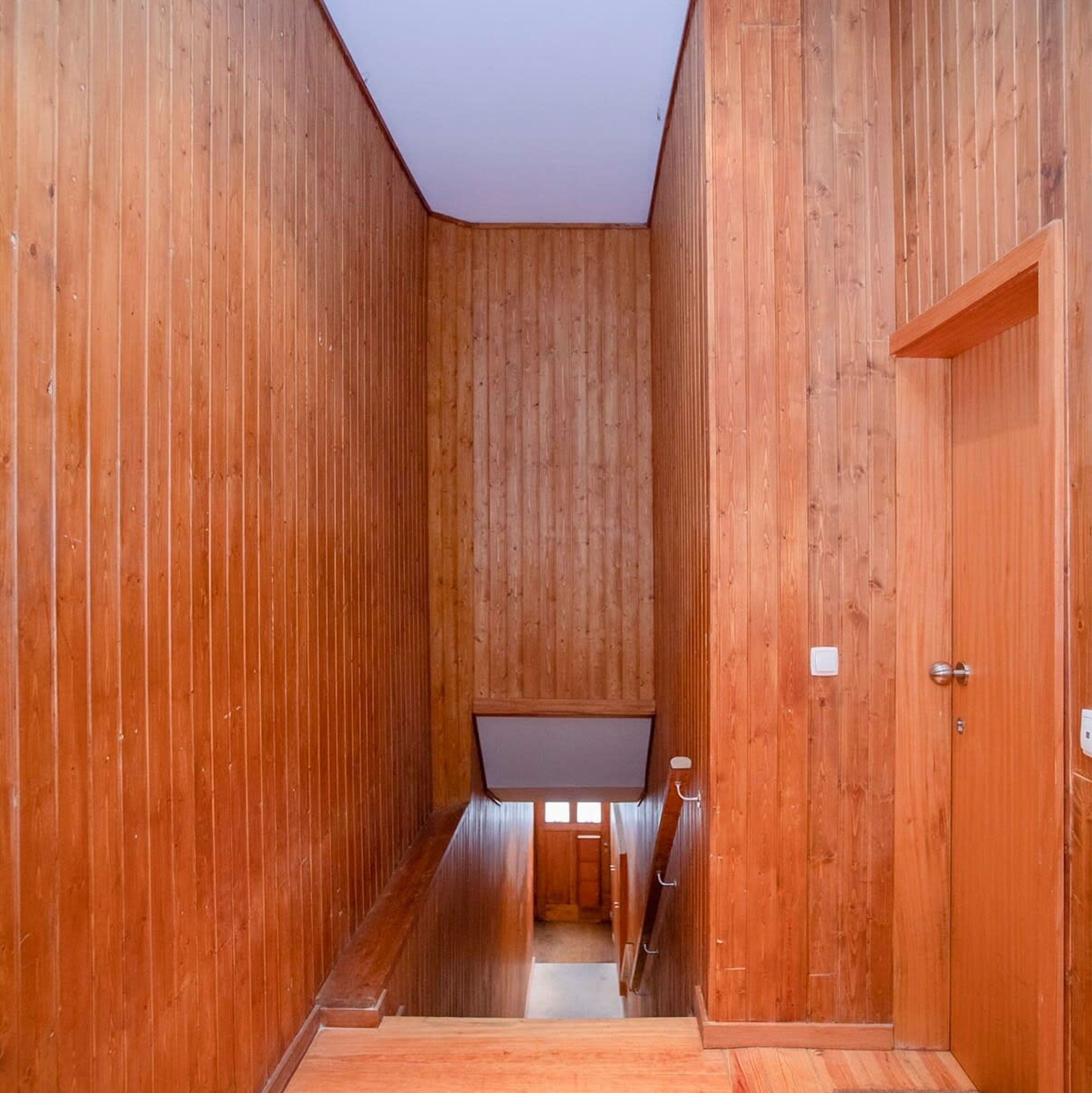 A narrow wooden hallway with a sloped ceiling and a door on the right.