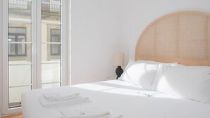 Hotellihuone, jossa on suuri sänky, puinen pääty, yöpöytä lampun kanssa ja näkymä ulos liukuoven kautta.