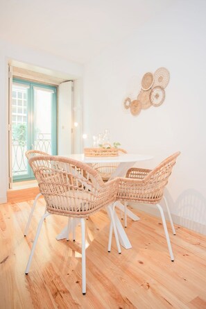 A dining area with wicker chairs and a white table, a door leading outside, and wall decor. - Liiiving in Porto - Boho Blue Home (Porto)