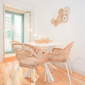 Un coin repas avec des chaises en osier et une table blanche, un panier contenant divers objets et un élément décoratif mural.