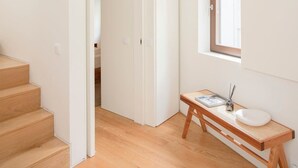 A modern, minimalist room with a wooden staircase, a white wardrobe, a small wooden table with a white sink, and a window providing natural light. - Liiiving in Porto - Cedofeita Green Terrace (Porto)