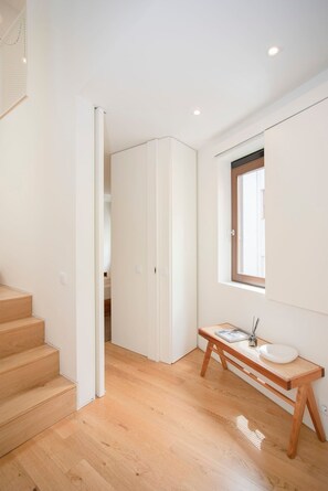 Ein modernes Interieur mit einer Holztreppe, einer weißen Tür, die in einen anderen Raum führt, und einem kleinen Tisch mit einem weißen Waschbecken und einem Fenster darüber.