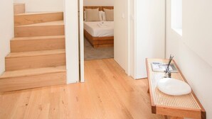 A modern hotel room with a wooden staircase, a bed with white bedding, a small bedside table with a white sink, and a window providing natural light. - Liiiving in Porto - Cedofeita Green Terrace (Porto)