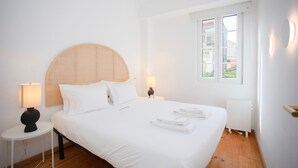 A hotel room with a large bed, two bedside lamps, a window with blinds, and a radiator. - Liiiving in Gaia - Casa da Vinha Apartment V (Vila Nova de Gaia)