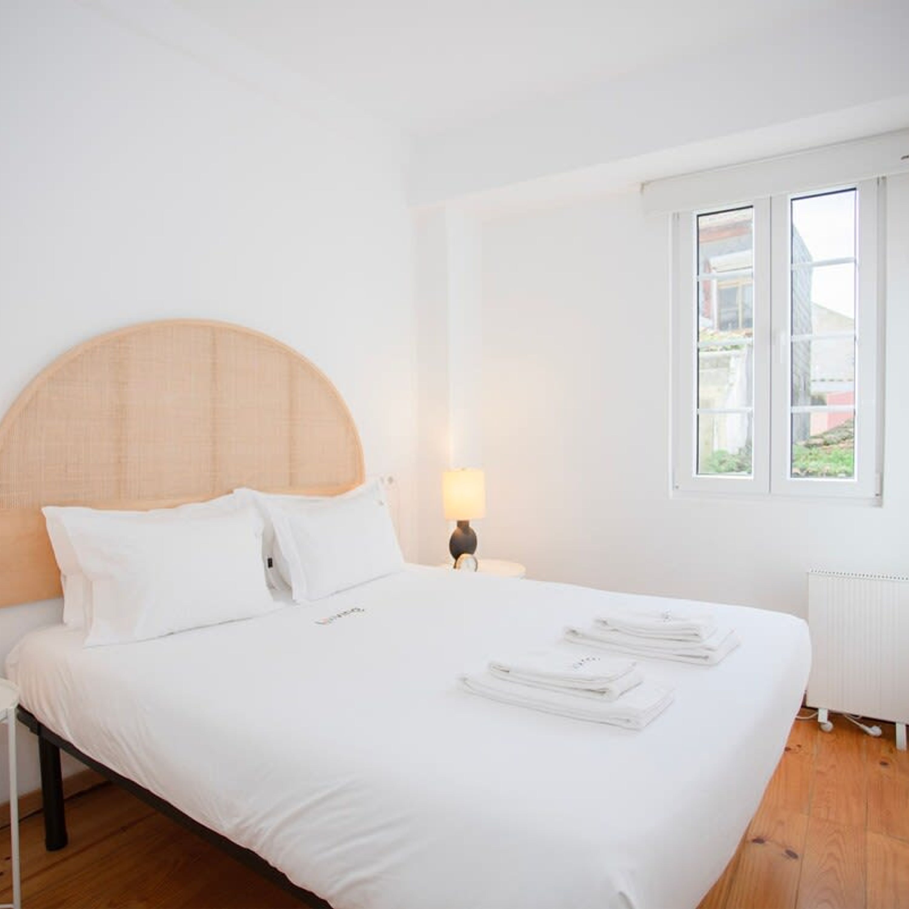 A neatly made bed with white linens, a wooden headboard, and a nightstand with a lamp.