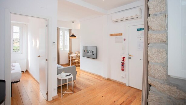 A modern hotel room with wooden flooring, a dining area with a table and chairs, a mounted TV, and a stone accent wall. - Liiiving in Gaia - Casa da Vinha Apartment V (Vila Nova de Gaia)