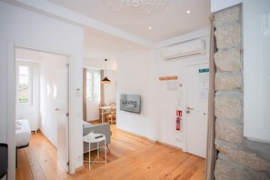 A modern hotel room with wooden flooring, a dining area with a table and chairs, a mounted TV, and a stone accent wall. - Liiiving in Gaia - Casa da Vinha Apartment V (Vila Nova de Gaia)