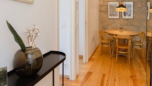 A modern interior with a wooden floor, a round dining table with chairs, a black console table with a vase, and framed artwork on the walls. - Liiiving in Gaia - Casa da Vinha Apartment VI (Vila Nova de Gaia)