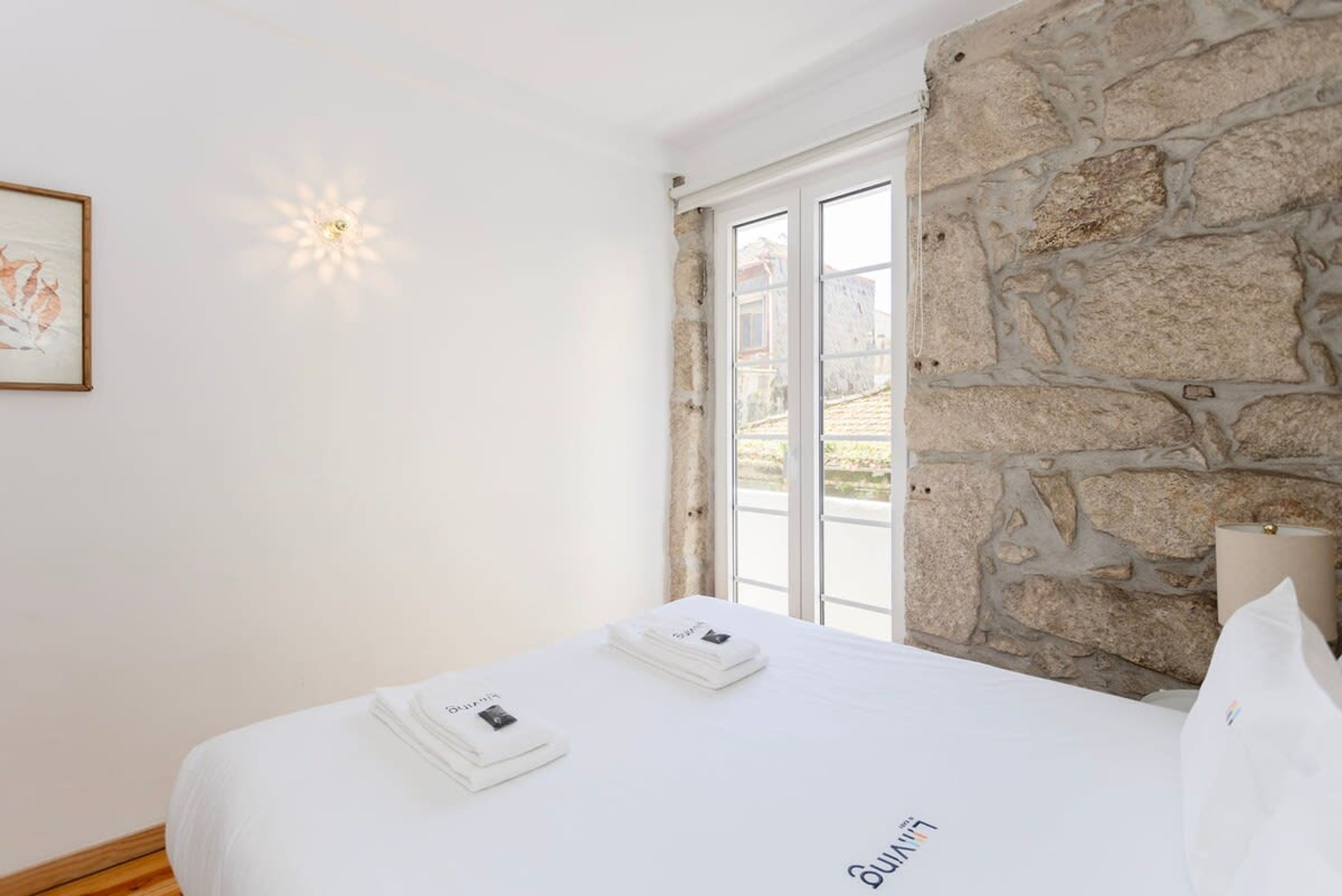 A hotel room with a stone wall, a bed with white linens, and a framed picture on the wall.