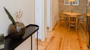 A modern dining area with a stone accent wall, wooden flooring, and a round table with chairs. - Liiiving in Gaia - Casa da Vinha Apartment VI (Vila Nova de Gaia)